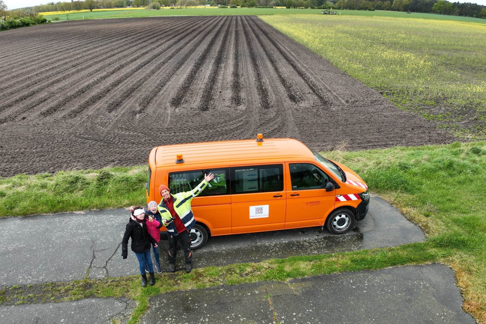 Zwei Schülerinnen waren am Zukunftstag bei der Abteilung Geoinformation, Foto von einer Drohne aufgenommen. Sie Mädchen stehen mit einem Mann vor einem orangenen VW-Bus. (Wird bei Klick vergrößert)